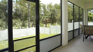Una habitación con ventanas amplias, una cerca blanca y una mesa con sillas.