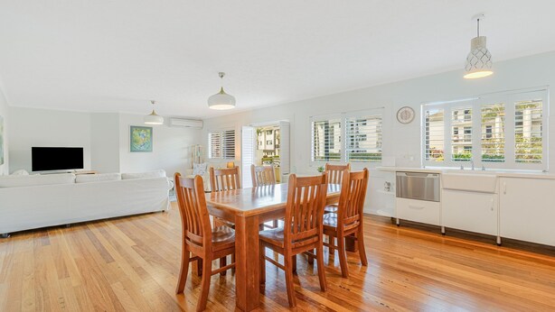 A modern kitchen with wooden flooring, white cabinetry, and a dining area with wooden chairs and a table.