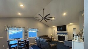Un salon spacieux doté d’une cheminée, d’un ventilateur de plafond et d’un coin repas avec une table et des chaises.