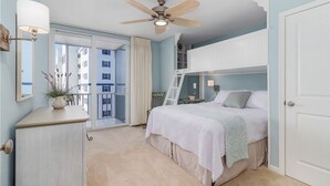Une chambre à coucher comprenant un lit, une commode, un ventilateur de plafond, une fenêtre avec des rideaux et un balcon.