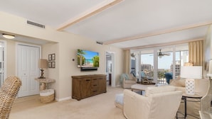 Un salon spacieux avec une grande télévision, un meuble en bois, un canapé beige et un balcon offrant une vue sur la ville.
