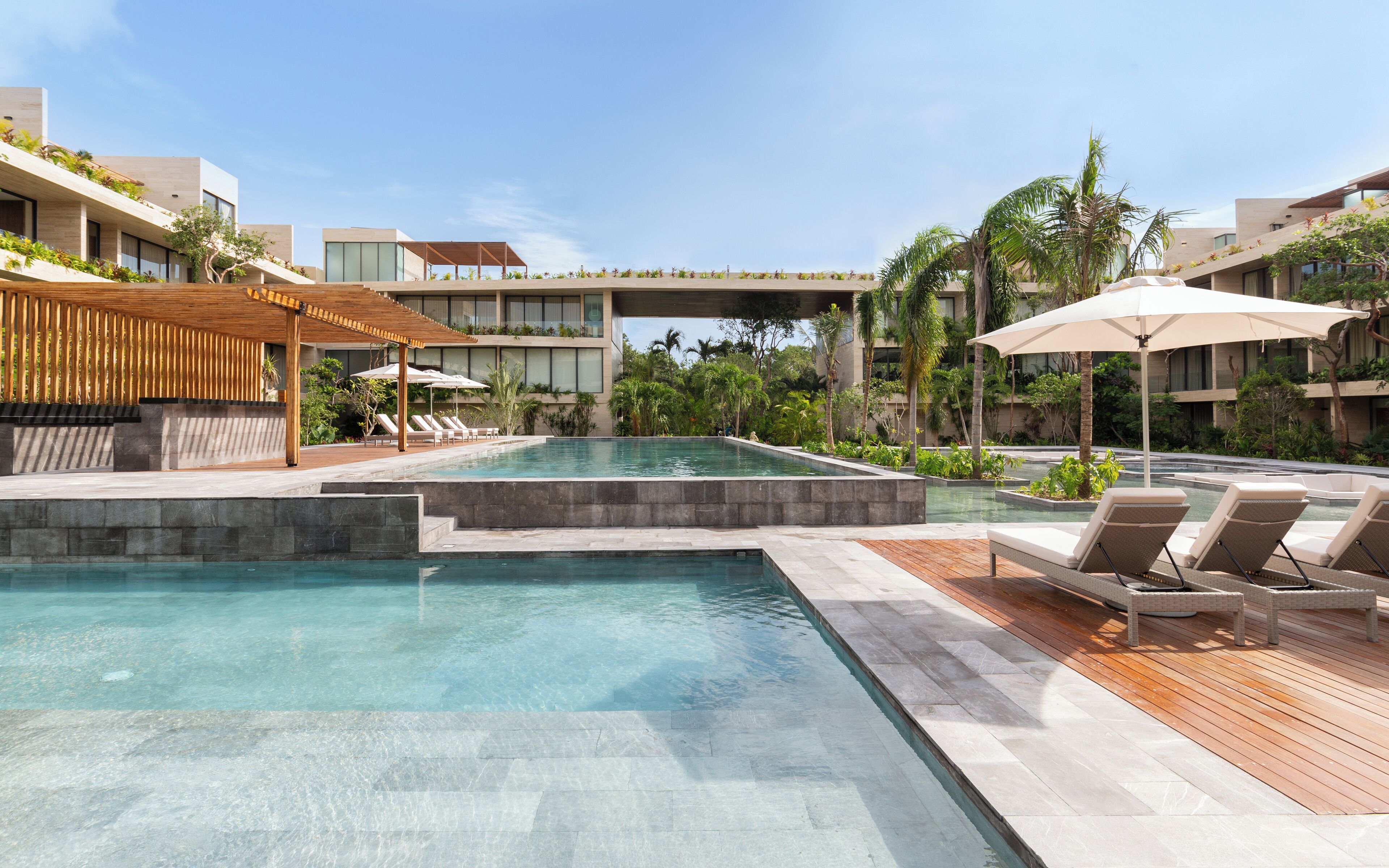 A modern hotel pool area with a clear pool, lounge chairs, and a wooden deck.