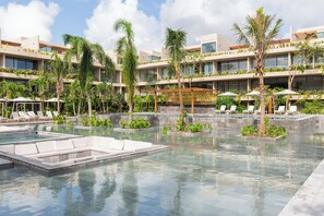 A resort pool area with multiple levels of buildings, lounge chairs, and palm trees. - Luxury 2Bed MT D104 By Sandy Powerful (Tulum)