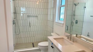 Et moderne badeværelse med en glasvæg omkring bruseren, toilet og et vaskeskab med spejl.