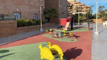 Ein Spielplatz mit roter und grüner Bodenfläche, gelben Klettergerüsten und einer roten Rutsche.