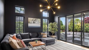 A modern living room with a sectional sofa, a coffee table, and a large window with a view of greenery. - Ocean Whisper Retreat (Victoria)