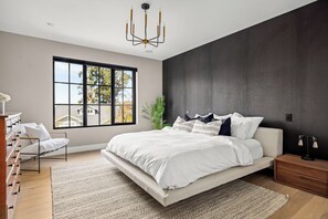 Ein modernes Schlafzimmer mit einem großen Bett, einem Ausblick durch ein Fenster und einer dunklen Akzentwand.