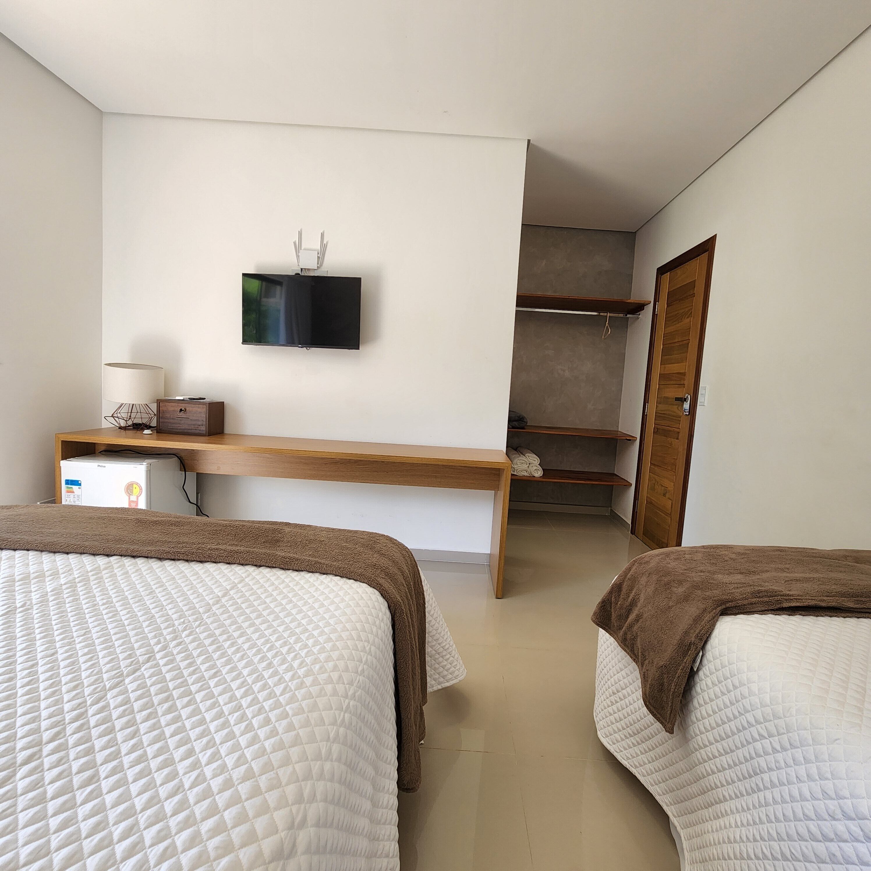 A bedroom with two beds, a desk, a television, and a wardrobe.
