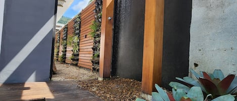 A modern outdoor area with a wooden deck, a black wall with vertical wooden slats, and a concrete pillar.