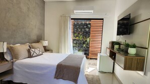 A modern bedroom with a large bed, bedside tables, a TV mounted on the wall, and a balcony with potted plants. - Rei dos Mares Suítes by Easy Hotéis (Ubatuba)