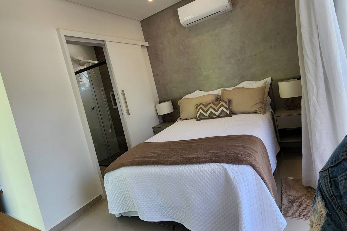 A modern bedroom with a bed, bedside lamps, a wardrobe, and an air conditioning unit.