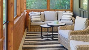 A cozy wooden room with a sofa and a small table, large windows, and a striped rug. - Little River Retreat (Townsend)