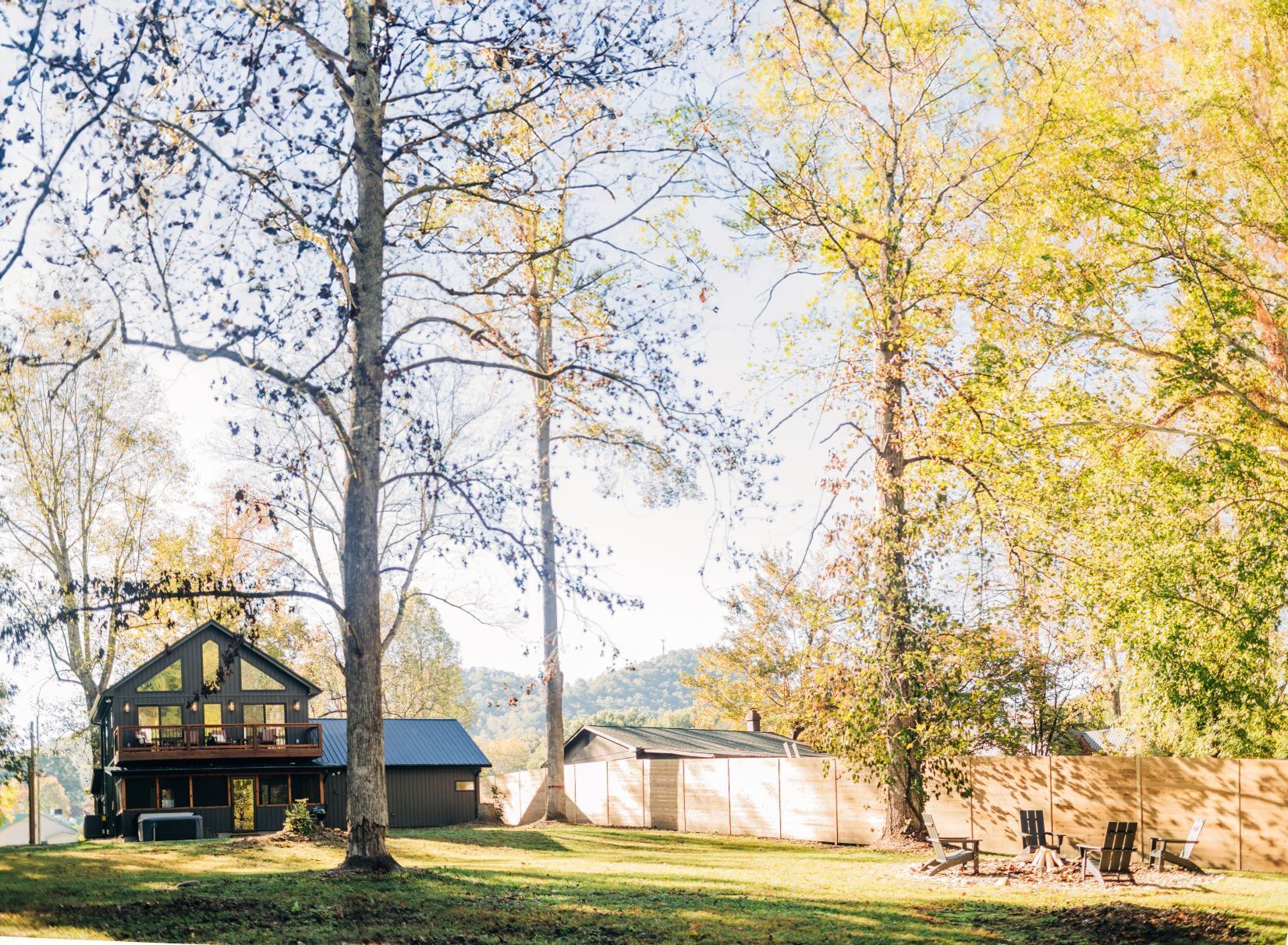 A two-story cabin with a balcony, surrounded by trees and a grassy yard.