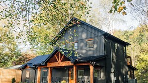 A large, dark wooden house with a steeply pitched roof, multiple windows, and a porch with chairs. - Little River Retreat (Townsend)