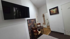 Una stanza piccola e funzionale con una TV a schermo piatto montata a parete, un tavolo da pranzo con sedie e una libreria piena di libri.