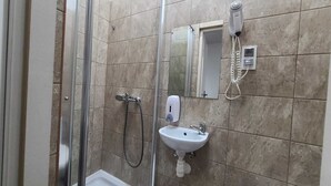 Un bagno con box doccia in vetro, un lavandino bianco, un asciugacapelli portatile e uno specchio.