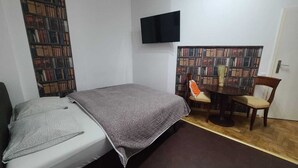 Una camera da letto con un letto, una TV a muro, una libreria e un tavolino con una sedia.