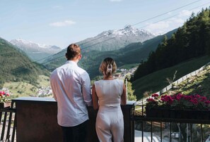 A couple standing on a balcony overlooking a mountainous landscape with a village below. - Grünwald Resort Sölden (Soelden)