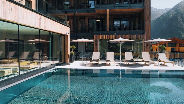 A modern hotel with a pool area, lounge chairs, and a mountain view. - Grünwald Resort Sölden (Soelden)