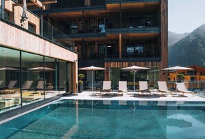 A modern hotel with a pool area, lounge chairs, and a mountain view.