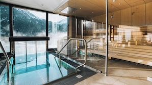 A modern indoor swimming pool with a glass barrier, wooden paneling, and a view of snow-capped mountains. - Grünwald Resort Sölden (Soelden)