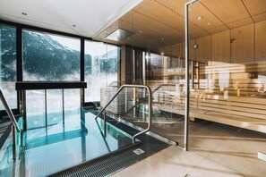 En modern inomhuspool med en glasvägg, träpanel och utsikt över snöklädda berg.