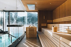 A modern sauna with wooden benches and a glass wall offering a mountain view.