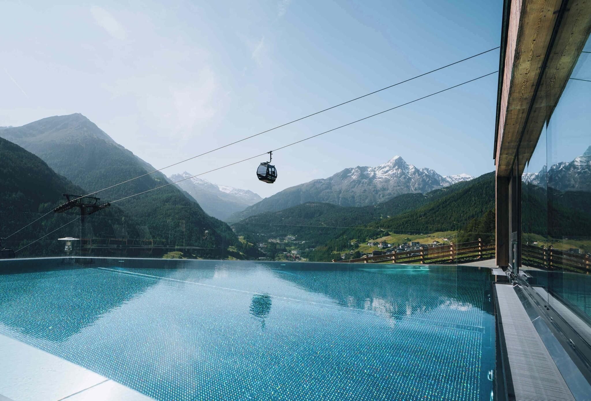 On aperçoit clairement une piscine, avec une télécabine en arrière-plan et des montagnes.