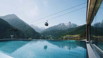 On aperçoit clairement une piscine, avec une télécabine en arrière-plan et des montagnes.