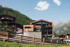 A modern mountain lodge with a stone facade, wooden balconies, and a view of the surrounding forest and mountains. - Grünwald Resort Sölden (Soelden)