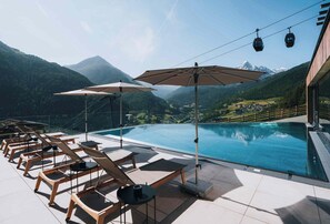 A poolside area with lounge chairs and umbrellas, overlooking a mountainous landscape.