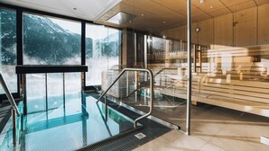 Une piscine intérieure moderne, dotée d’une paroi en verre, d’un lambris en bois et offrant une vue sur des montagnes enneigées.