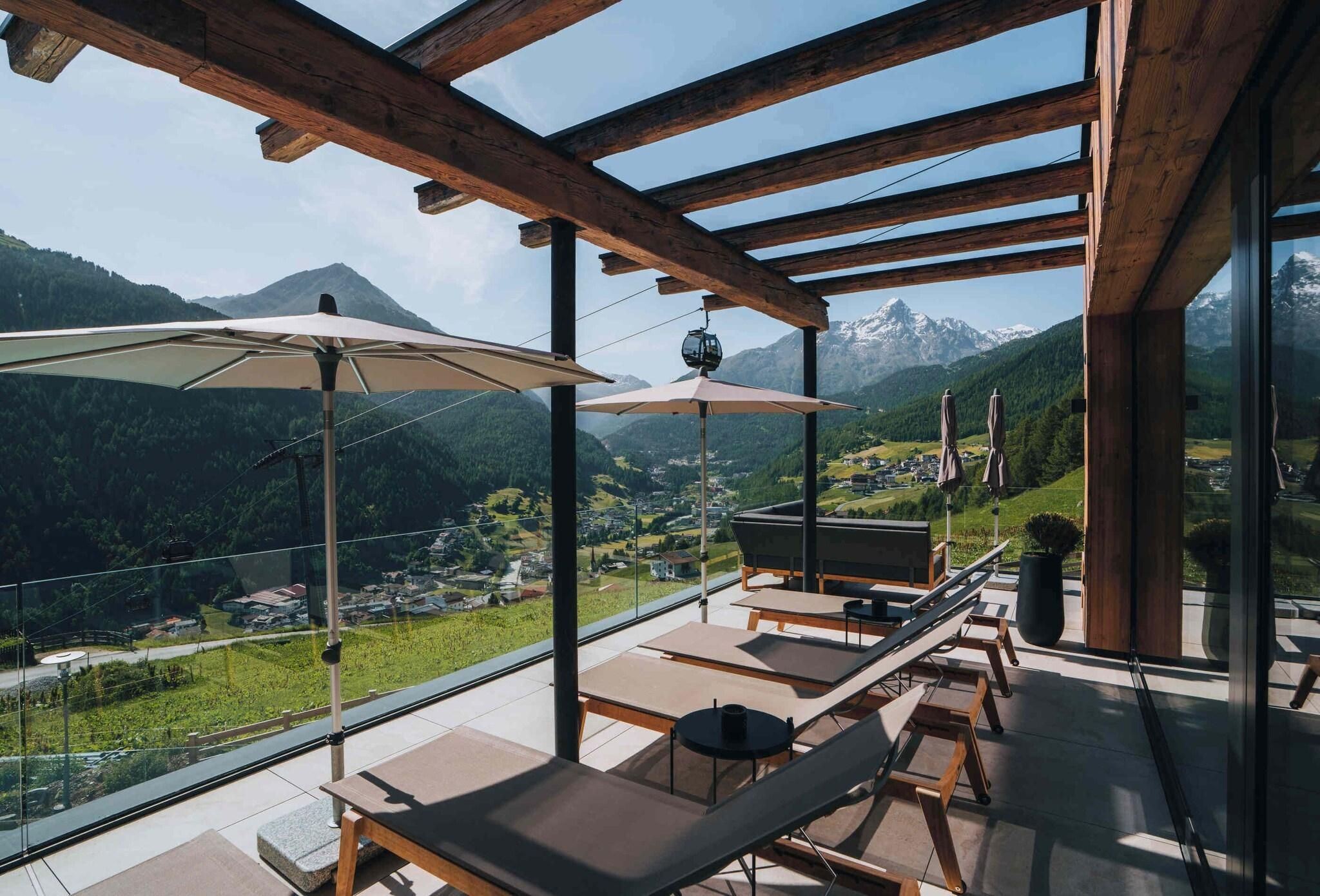 Un balcone con travi in legno, poltrone da relax e ombrelloni con vista su un paesaggio montuoso.