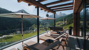 A balcony with wooden beams, lounge chairs, and umbrellas overlooking a mountainous landscape. - Grünwald Resort Sölden (Soelden)