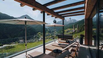 Un balcone con travi in legno, poltrone da relax e ombrelloni con vista su un paesaggio montuoso.