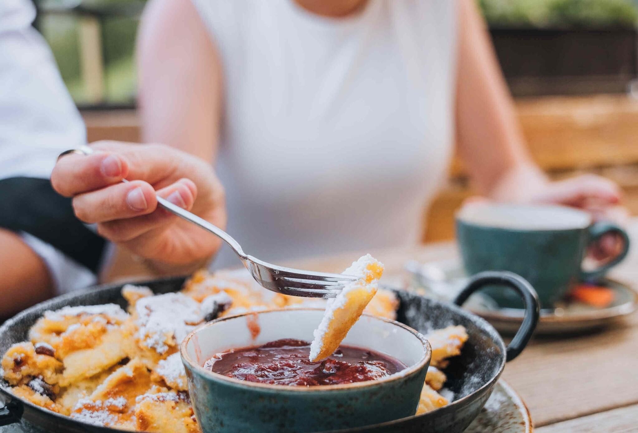 Une personne servant un dessert à l’aide d’une cuillère, avec un bol de sauce et une tasse placés sur une table.