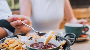 Une personne servant un dessert à l’aide d’une cuillère, avec un bol de sauce et une tasse placés sur une table.