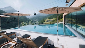 A rooftop infinity pool with lounge chairs and umbrellas, overlooking a mountainous landscape. - Grünwald Resort Sölden (Soelden)