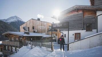 Un comprensorio sciistico con edifici in legno, un segnale che indica l'accesso diretto alle piste e una persona con abbigliamento da neve.