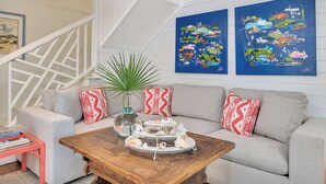 A living room with a grey sofa, red and white patterned pillows, a wooden coffee table with seashells, and two blue paintings on the wall.
