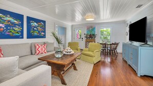 A living room with a sofa, armchairs, a coffee table, and a TV in a modern setting with wooden floors and white walls.