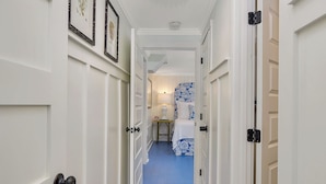 A hallway with white doors, a blue carpet, and a bed with blue and white bedding.