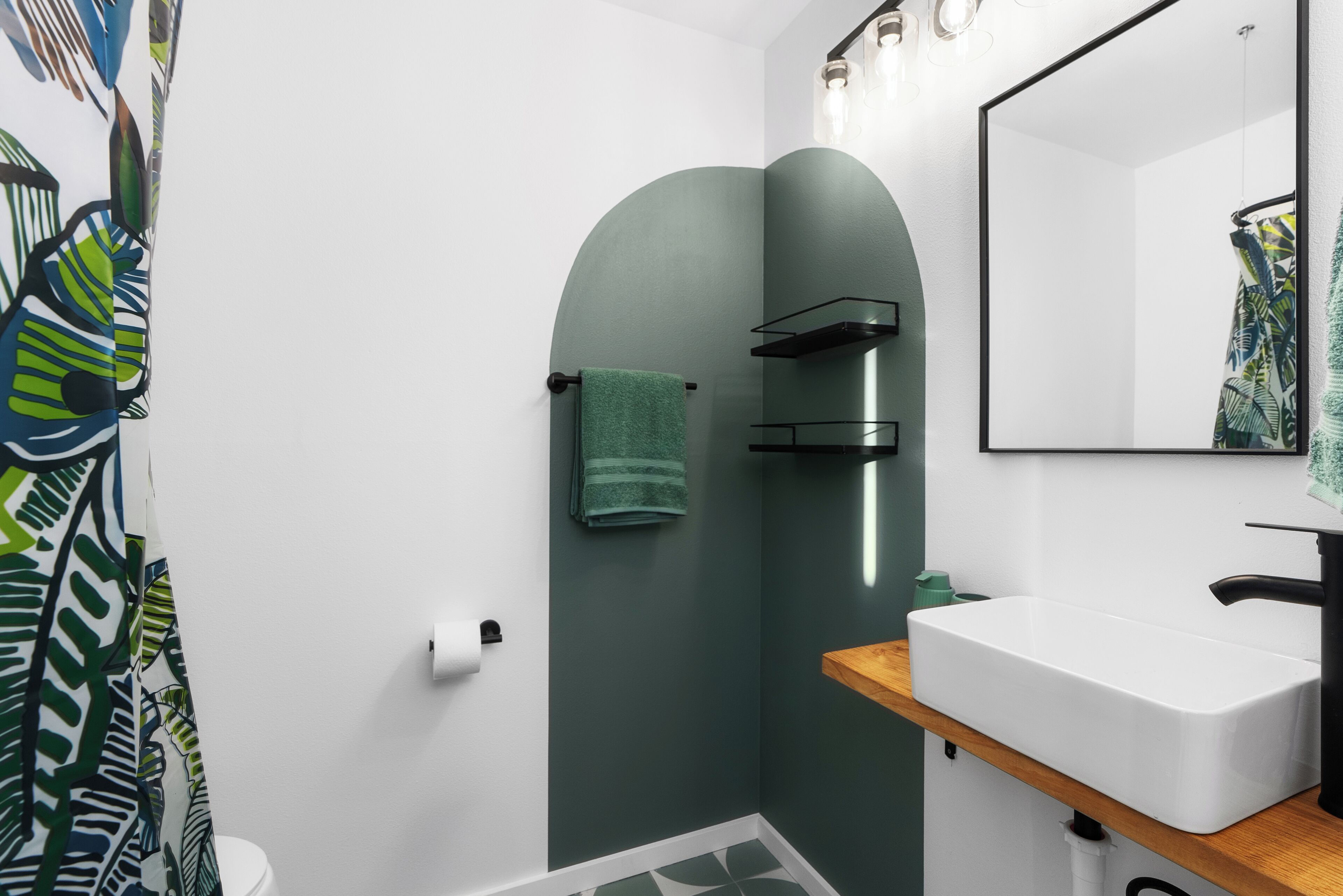 Ein Badezimmer mit einem weißen Waschbecken, einem Spiegel, einem grünen Handtuch und einer Dusche mit grüner Wand.