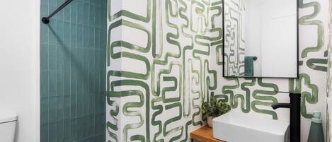 A bathroom with a green patterned shower curtain, a white sink, and a mirror on the wall.