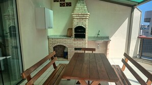 Eine Terrasse mit Backofen aus Ziegeln, Holzbanken und ein Fliesenboden.
