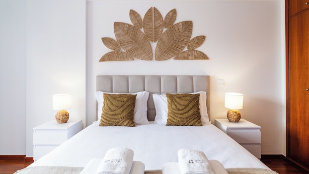 A neatly made bed with two pillows, two bedside lamps, and a wall art piece above the bed.