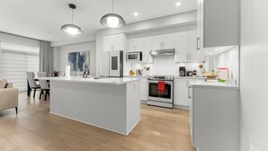 Una cucina moderna con mobili bianchi, un'isola centrale, elettrodomestici in acciaio inossidabile e un'area pranzo con divano e sedie.