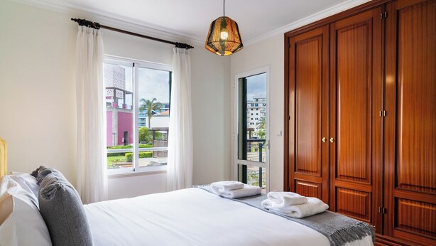 A hotel room with a bed, a wardrobe, and a window with curtains. - GuestReady - Lovely experience in Funchal (Funchal)
