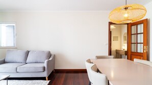 A modern living room with a grey sofa, a wooden dining table with chairs, a woven pendant light, and a wooden floor. - GuestReady - Lovely experience in Funchal (Funchal)