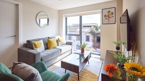 A living room with a grey sofa, green armchair, and a coffee table. There is a large window with a view of buildings outside. - GG-Guest House (Liverpool)